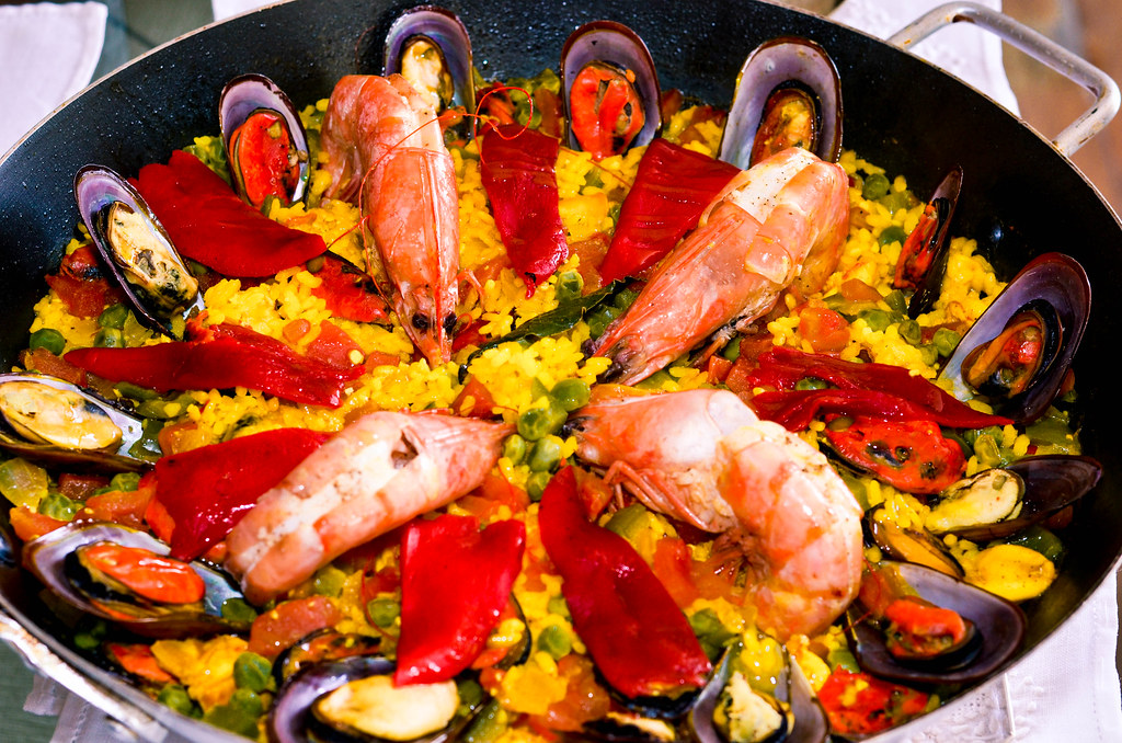 Paella espagnole traditionnelle aux fruits de mer, servie dans une grande poêle noire avec crevettes, moules et légumes colorés.