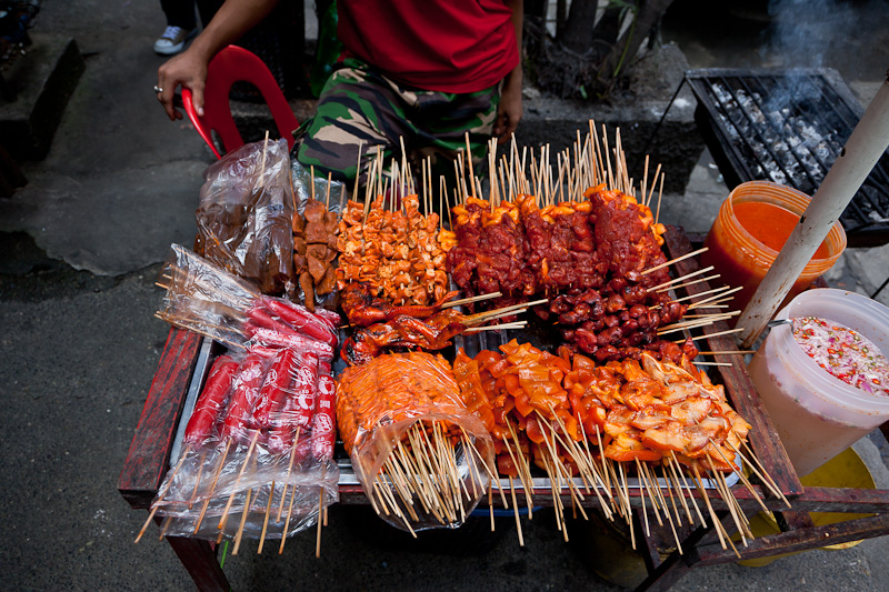Une variété de brochettes de viande et de saucisses présentées sur un stand de street food.