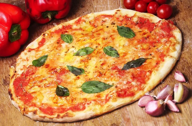 Assortiment de plats traditionnels italiens comprenant une pizza napolitaine, des pâtes carbonara et un tiramisu, servis sur une table en bois.