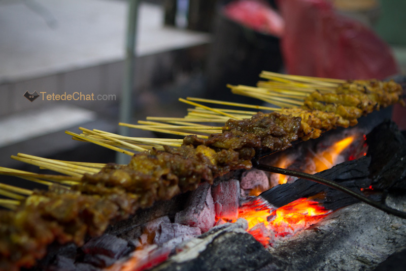Vendeur de street food préparant des brochettes de porc dans un marché de nuit à Bangkok”