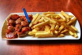 Currywurst servie dans une assiette en carton avec sauce au curry, spécialité allemande populaire à Berlin